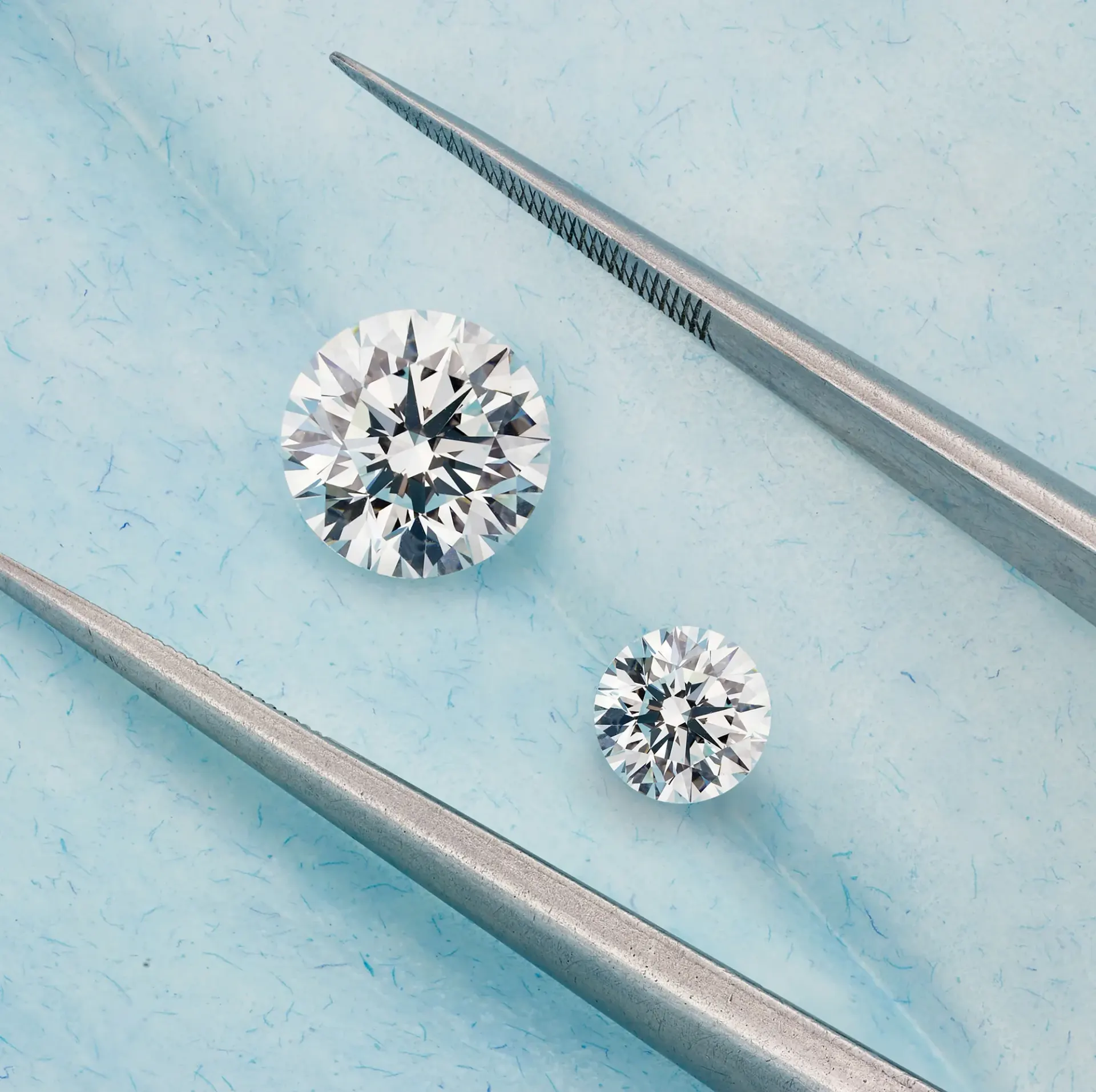Two loose round-brilliant diamonds beside jeweler’s tweezers.