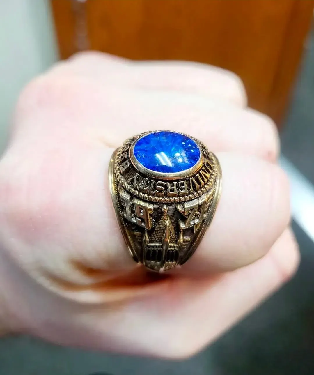 A yellow-gold university class ring with a blue spinel center stone.