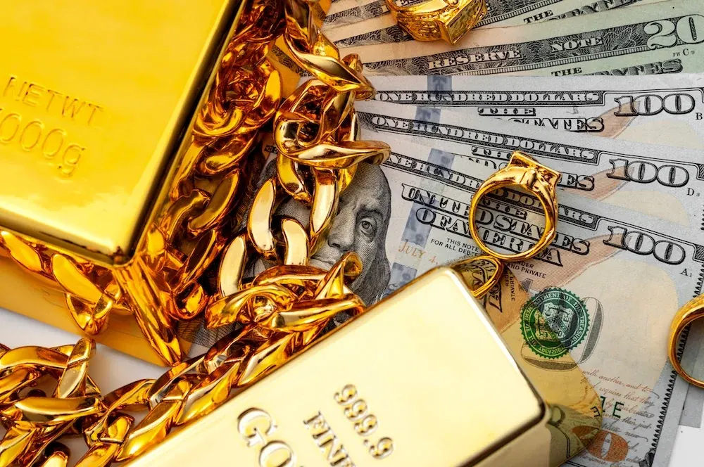 Gold bars, chains, and a ring resting on hundred-dollar bills.