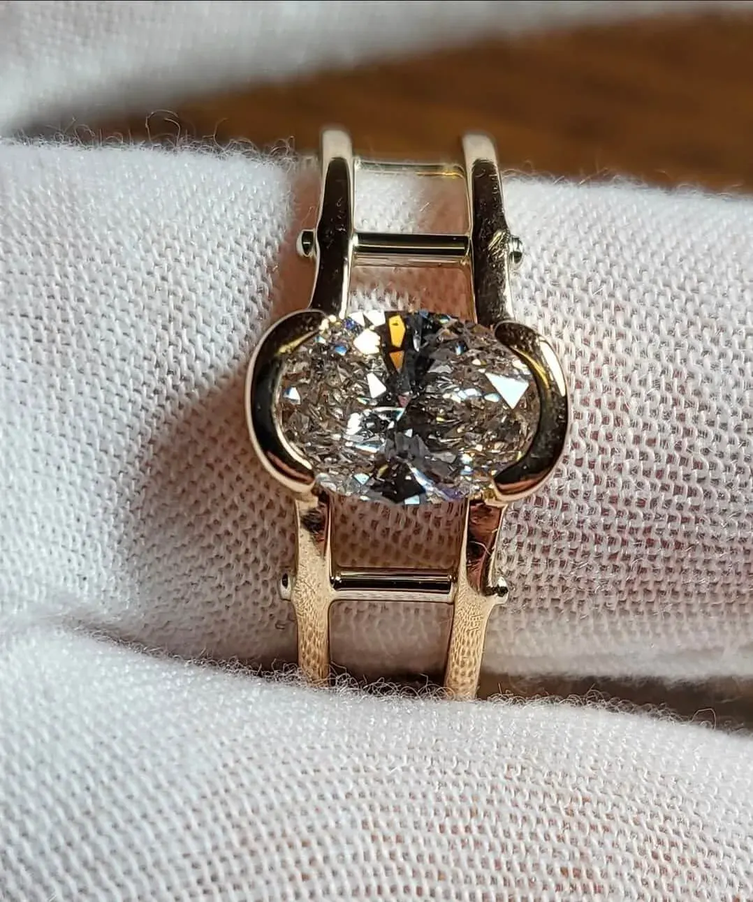 An oval diamond solitaire in a half-bezel rose-gold setting.